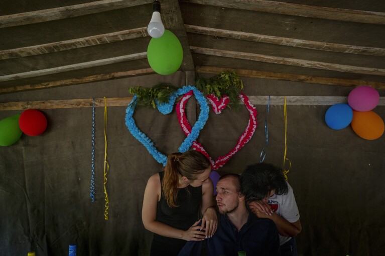 Blind Ukrainian soldier Ivan Soroka, center, is surrounded by his wife Vladislava Ryabets, left, and his mother-in-law during the second day of his wedding in the outskirt of Kyiv, Ukraine on Sunday, Sept. 10, 2023. (AP Photo/Bela Szandelszky)