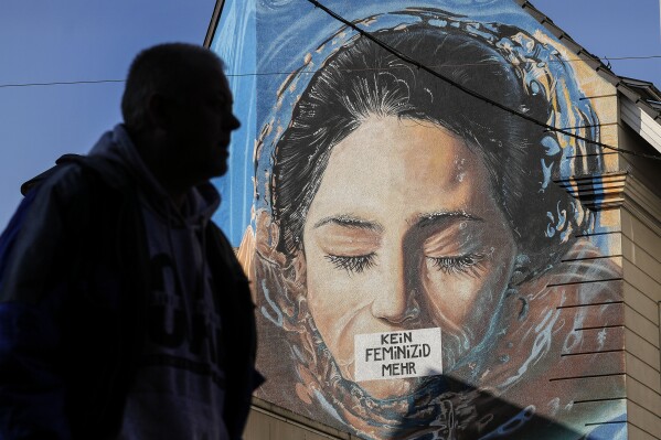 A man walks past a large protest painting against hate crime against women, reading "no more femicide" at a house wall in Gelsenkirchen, Germany, on the International Women's Day, Friday, March 8, 2024. Marches, demonstrations and conferences are being held the world over, from Asia to Latin America and elsewhere to mark International Women's Day. (AP Photo/Martin Meissner)