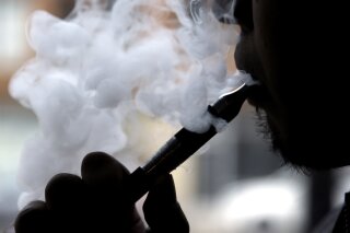 FILE - In this April 23, 2014 file photo, a man smokes an electronic cigarette in Chicago. Teen vapers prefer Juul and mint is the #1 flavor among many of them, suggesting a shift after the company’s fruit and dessert flavors were removed from retail stores, new U.S. research suggests. The results are in a pair of studies published Tuesday, Nov. 5, 2019, including a report from the Food and Drug Administration and federal Centers for Disease Control and Prevention indicating that the U.S. teen vaping epidemic shows no signs of slowing down. (AP Photo/Nam Y. Huh, File)