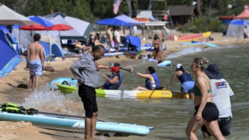 A man wets his feet in the cool water of Lake Tahoe at Lake Tahoe Nevada State Park in Incline Village, Nev., Monday, July 17, 2023. Tourism officials at Lake Tahoe were surprised, and a bit standoffish, when a respected international travel guide included the iconic alpine lake straddling the California line on a list of places to stay away from this year because of the harmful ecological effects of “over-tourism.” (AP Photo/Andy Barron)