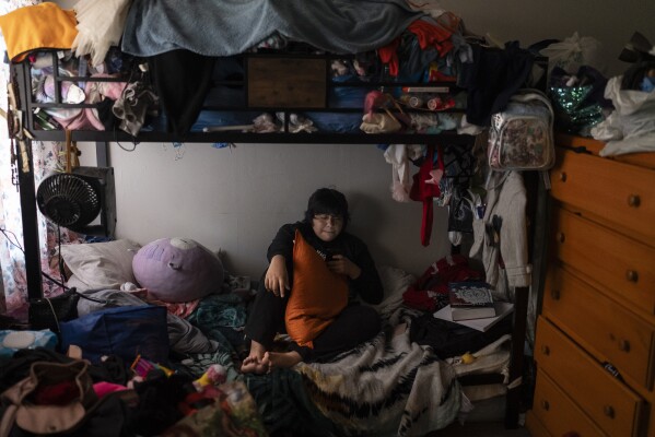 Deneffy Sánchez, 15, rests on a bed he shares with his mother and little sister just feet away from their roommate's bed in Los Angeles, Saturday, Sept. 9, 2023. In Los Angeles, housing insecurity is one of the biggest reasons kids have missed school since the pandemic and struggle to catch up. (AP Photo/Jae C. Hong)