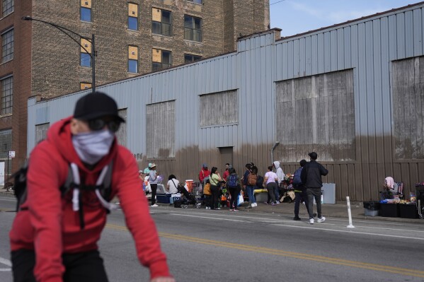 People hang around outside of a migrant shelter Wednesday, March 13, 2024, in the Pilsen neighborhood of Chicago. Multiple people living at the shelter for migrants have tested positive for measles since last week. A team from the Centers for Disease Control and Prevention is supporting local officials' response. (AP Photo/Erin Hooley)