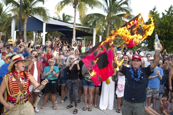 In this photo provided by the Florida Keys News Bureau, Jai Somers, left, holds hurricane warning flags aloft as they burn after being doused with rum by Paul Menta, right, to mark the end of the 2023 Atlantic hurricane season Thursday, Nov. 30, 2023, in Key West, Fla. According to the National Hurricane Center, this year's above-normal Atlantic hurricane season was characterized by record warm Atlantic Ocean sea surface temperatures and a strong El Nino. The Atlantic basin saw 20 named storms in 2023. (Carol Tedesco/Florida Keys News Bureau via AP)