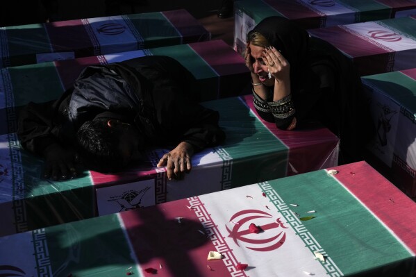 Mourners weep over the flag-draped coffin of their loved one who was killed in Wednesday's bomb explosion, during the victims funeral ceremony in the city of Kerman about 510 miles (820 kms) southeast of the capital Tehran, Iran, Friday, Jan. 5, 2024. Iran on Friday mourned those slain in an Islamic State group-claimed suicide bombing targeting a commemoration for a general slain in a U.S. drone strike in 2020. (AP Photo/Vahid Salemi)