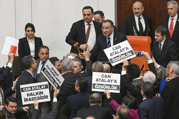 Turkish lawmakers, few holding up boards that read in Turkish: "Freedom for Can Atalay" argue with Parliament Deputy speaker Bekir Bozdag, top center, during a session at the Turkish parliament in Ankara, Tuesday, Jan. 30, 2024. The Turkish Parliament stripped an imprisoned opposition lawmaker Can Atalay of his parliamentary status on Tuesday, defying a ruling made by the country's top court in September. Other boards read in Turkish: "Can Atalay. It's the will of the people". (Mert Gokhan Koc/Dia Images via AP)