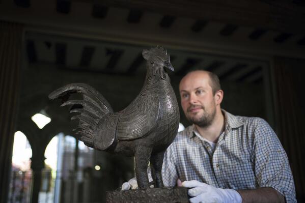 Archivist Robert Athol looks at a bronze statue of a cockerel called The Okukor, one of the Benin Bronzes, at Jesus College, University of Cambridge, England, Friday Oct. 15, 2021. The Cambridge University college will return a looted bronze cockerel to Nigeria later this month, making it the first U.K. institution to hand back one of the artifacts known as the Benin Bronzes. (Joe Giddens/PA via AP)