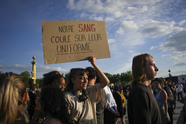 A woman holds a placard reading "Our blood runs on their uniform" during a protest in Paris, France, Friday, June 30, 2023. French President Emmanuel Macron urged parents Friday to keep teenagers at home and proposed restrictions on social media to quell rioting spreading across France over the fatal police shooting of a 17-year-old driver. (AP Photo/Lewis Joly)