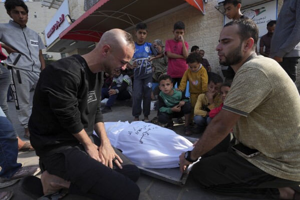 Palestinians mourn over the body of their father, Mohsem al Hegi, who was killed in the Israeli bombardment of the Gaza Strip, in front of the morgue of al Aqsa Hospital in Deir al Balah, Gaza Strip, Monday, Nov. 13, 2023. (AP Photo/Adel Hana)