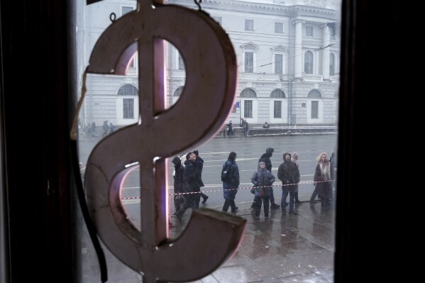 People stand near a currency exchange office waiting for municipal workers to finish clearing snow and ice from the roof of the building in St. Petersburg, Russia, Tuesday, Feb. 18, 2025. (AP Photo/Dmitry Lovetsky)