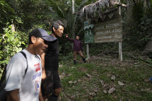 A group of men pass in front of a sign announcing the limit of Cordillera Azul National Park in Peru's Amazon, Monday, Oct. 3, 2022. (AP Photo/Martin Mejia, File)