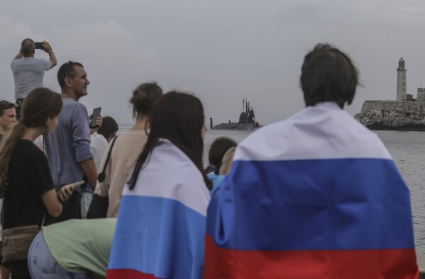 People wearing Russian flags watch the Russian Kazan nuclear-powered submarine arrive at the port of Havana, Cuba, Wednesday, June 12, 2024. A fleet of Russian warships arrived in Cuban waters Wednesday ahead of planned military exercises in the Caribbean. (AP Photo/Ariel Ley)