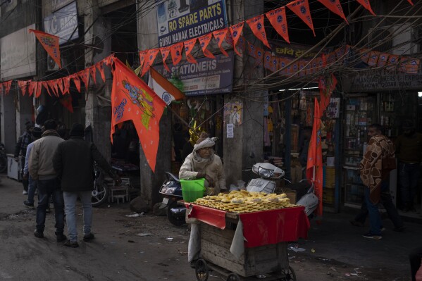 An elderly man selling pineapples waits for customers at a market decorated with flags featuring Hindu god Ram, in New Delhi, India, Tuesday, Jan. 16, 2024. (AP Photo/Altaf Qadri)