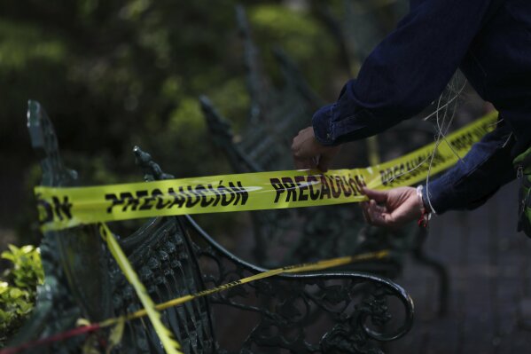 A municipal employee loops caution tape around park benches to discourage people from sitting on them in the main plaza of Coyoacan, in Mexico City, Saturday, April 4, 2020. Mexico has started taking tougher measures against the new coronavirus, but some experts warn the country is acting too late and testing too little to prevent the type of crisis unfolding across the border in the United States. (AP Photo/Fernando Llano)
