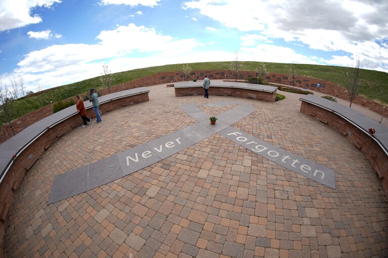 In this photograph taken through a fisheye lens, people visit the Columbine Memorial, Wednesday, April 17, 2024, in Littleton, Colo. Trauma still shadows the survivors of the horrific Columbine High School shooting as the attack's 25th anniversary approaches. (AP Photo/David Zalubowski)