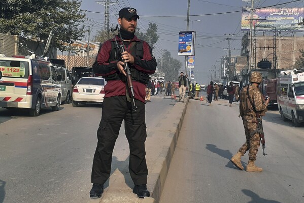 Police and army soldiers cordon off an area following a bomb explosion, in Peshawar, Pakistan, Tuesday, Dec. 5, 2023. A roadside bomb went off near a school in northwestern Pakistan on Tuesday, wounding a few children and damaging windows of a nearby bank and shops, police and a rescue official said. (AP Photo/Muhammad Sajjad)