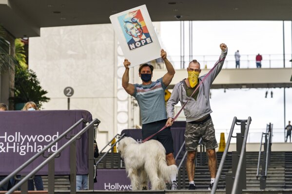 Lindsay Farmer, left, and Florian Klein, holding their dog, "Sophie," hold a "Nope" poster as they celebrate Saturday, Nov. 7, 2020, at Highland & Hollywood in Los Angeles, after Democrat Joe Biden defeated President Donald Trump to become 46th president of the United States. (AP Photo/Damian Dovarganes)