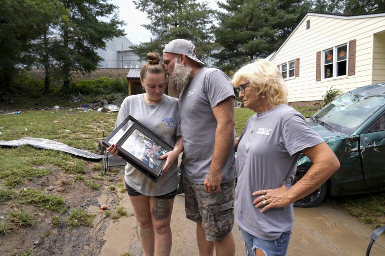 Dustin Bentley, center, kisses his wife, Jennifer Bentley, left, after retrieving family photos from their flood damaged home as his mother Janet Sams looks on Saturday, Sept. 28, 2024, in Newport, Tenn. (AP Photo/George Walker IV)