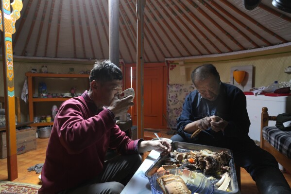 Herder Lkhaebum and his son, Agvaantogtokh, have breakfast before starting their day at a new pasture in the Munkh-Khaan region of the Sukhbaatar district in southeast Mongolia, Monday, May 16, 2023. (AP Photo/Manish Swarup)