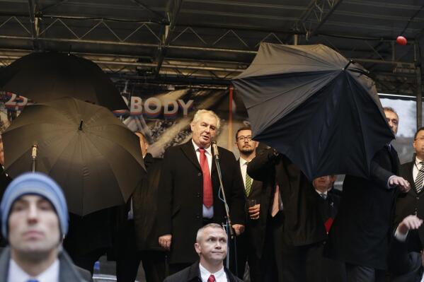 Security personnel use umbrellas to protect Czech Republic's President Milos Zeman, center, during his speech commemorating the 1989 anti-communist Velvet Revolution in Prague, Czech Republic, Monday, Nov. 17, 2014. During the ceremony protesters booed and pelt objects such as sandwiches, tomatoes and eggs towards the Czech President to protest his demeaning of importance of human rights, a pro-Russian stance in the conflict in Ukraine, using vulgar language and recently downplaying the brutal use of force by police 25 years ago. (AP Photo/Petr David Josek)