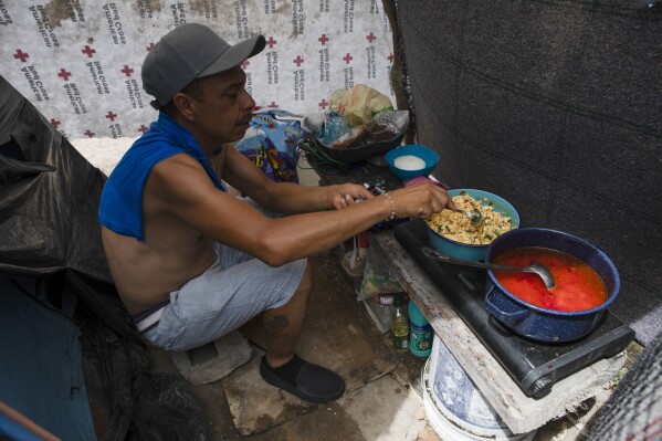 A migrant prepares a meal at a shelter encampment in the border town of Matamoros, Mexico, Wednesday, Aug. 16, 2023. Mexico’s immigration agency and a Catholic aid group have opened a temporary outdoor shelter for migrants living in camps to move to, as Mexico’s National Institute for Migration wants this large camp in Matamoros dismantled. (AP Photo/Jacky Muniello)