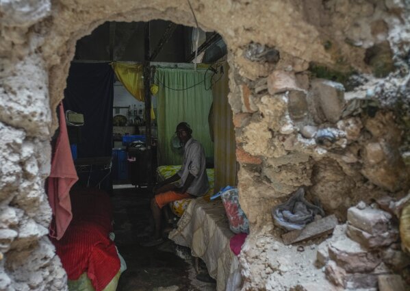 Mario Luis Poll sits for a photo on his bed behind a broken wall inside a partially destroyed mansion where he lives with five other families on Villegas Street in Havana, Cuba, Thursday, Oct. 5, 2023. (AP Photo/Ramon Espinosa)