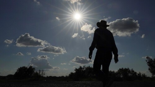 FILE - Kayak and canoe outfitter Jessie Fuentes walks along the Rio Grande under a warm sun Thursday, July 6, 2023. As the heat breaks records, weakening and sickening people, it’s worth remembering that dire heat waves have inspired effective efforts to prevent heat illness. (AP Photo/Eric Gay, File)