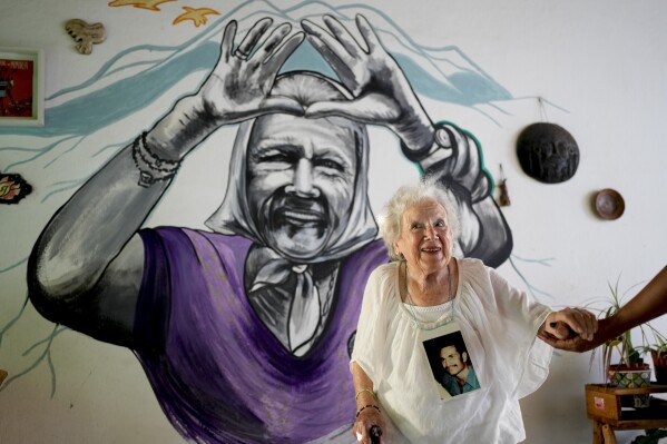 Nora Cortinas, 94, poses for a portrait wearing a photo of her disappeared son Gustavo at her home, decorated with a mural of her, on the outskirts of Buenos Aires, Argentina, Monday, Jan. 29, 2024. Cortinas became one of many mothers whose children were kidnapped by the state when Gustavo disappeared on April 15, 1977, giving birth to what is today's human rights organization, the Mothers of Plaza de Mayo. (AP Photo/Natacha Pisarenko)