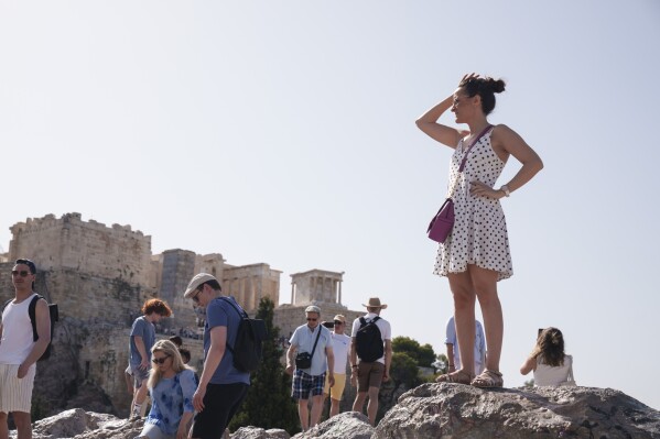 Tourists stand at the Aeropagous hill in front of the ancient Acropolis, in central Athens, Wednesday, June 12, 2024. The ancient site of Acropolis will be closed to the public for five hours due to a heat wave that pushed temperatures to 39 degrees Celsius (102 Fahrenheit) in the capital and even higher in parts of central Greece. (AP Photo/Petros Giannakouris)