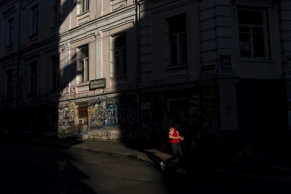 A woman walks past a building lit by a shaft of light in Kyiv, Ukraine, Tuesday, July 4, 2023. (AP Photo/Jae C. Hong)
