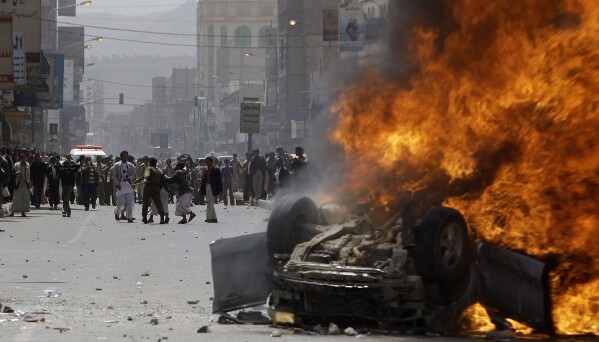 A Yemeni police officer stops supporters of the Yemeni government from reaching a vehicle set on fire by anti-government demonstrators during clashes in Sanaa, Yemen, on Feb. 22, 2011. (AP Photo/Muhammed Muheisen, File)
