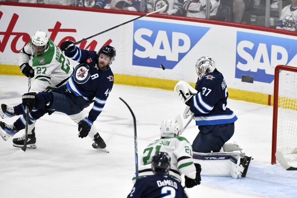 Winnipeg Jets goaltender Connor Hellebuyck (37) makes a save as Dallas Stars' Mason Marchment (27) dumps Jets' Josh Morrissey (44) during the first period of Game 2 of a second-round NHL hockey playoff series in Winnipeg, Manitoba, Friday, May 9, 2025. (Fred Greenslade/The Canadian Press via AP)
