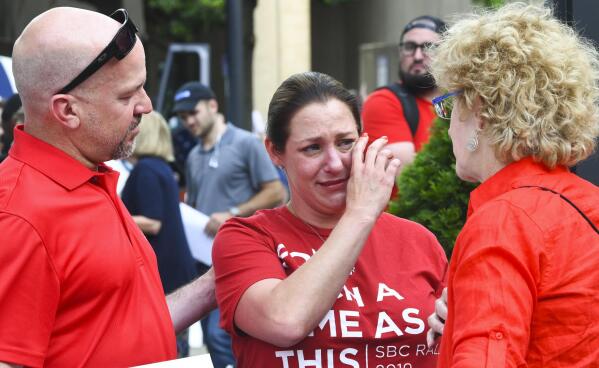 FILE - In this Tuesday, June 11, 2019 file photo, Jules Woodson, center, of Colorado Springs, Colo., is comforted by her boyfriend Ben Smith, left, and Christa Brown during a demonstration outside the Southern Baptist Convention's annual meeting in Birmingham, Ala. First-time attendee Woodson spoke through tears as she described being abused sexually by a Southern Baptist minister. A blistering report on the Southern Baptist Convention’s mishandling of sex abuse allegations, released on Sunday, May 23, 2022, is raising the prospect that the denomination, for the first time, will create a publicly accessible database of pastors and other church personnel known to be abusers. (AP Photo/Julie Bennett, File)