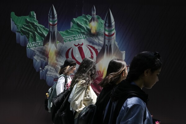 Iranian women walk past a banner showing missiles being launched from Iranian map in northern Tehran, Iran, April 19, 2024. (AP Photo/Vahid Salemi)