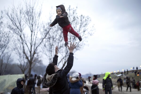 A migrant throws a baby in the air in Edirne near the Turkish-Greek border on Thursday, March 5, 2020. Turkey said Thursday it would deploy special forces along its land border with Greece to prevent Greek authorities from pushing back migrants trying to cross into Europe, after Turkey declared its previously guarded gateways to Europe open. (AP Photo/Emrah Gurel)