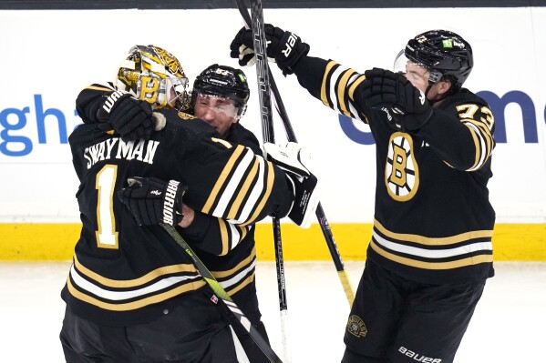 Boston Bruins goaltender Jeremy Swayman (1) is embraced by Brad Marchand as Charlie McAvoy, right, skates in for a hug following a shootout during NHL hockey game, Monday, Feb. 19, 2024, in Boston. Both Marchand and McAvoy scored in the shootout as the Bruins defeated the Stars. (AP Photo/Charles Krupa)