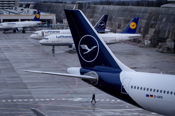 FILE - A person walks near parked Lufthansa aircrafts at the airport in Frankfurt, Germany, on March 26, 2023. A union has called on Lufthansa's ground staff to walk off the job for a day on Wednesday in a pay dispute, the latest of several transport strikes in the country. The Ver.di union said Monday it is calling on ground staff for the German airline at Frankfurt, Munich, Hamburg, Berlin and Duesseldorf airports to strike from 4 a.m. Wednesday. (AP Photo/Michael Probst, File)