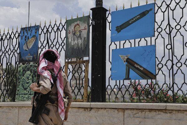 Một tay súng Yemen đi ngang qua những bức tranh mô tả tên lửa và cảnh đoàn kết với Gaza, được trưng bày trên hàng rào ven đường ở Sanaa, Yemen, thứ Hai, ngày 5 tháng 5 năm 2025. (Ảnh AP/Osamah Abdulrahman)