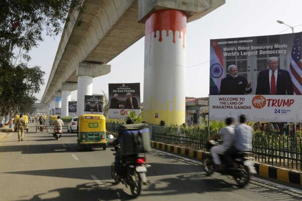 In this Feb. 21, 2020, photo, commuters move past hoardings welcoming U.S. President Donald Trump near Sardar Patel stadium in Ahmedabad, India. A festive mood has enveloped Ahmedabad in India’s northwestern state of Gujarat ahead of Prime Minister Narendra Modi's meeting Monday with U.S. President Donald Trump, whom he's promised millions of adoring fans. The rally in Modi's home state may help replace his association with deadly anti-Muslim riots in 2002 that landed him with a U.S. travel ban. It may also distract Indians, at least temporarily, from a slumping economy and ongoing protests over a citizenship law that excludes Muslims, but also risks reopening old wounds. (AP Photo/Ajit Solanki)