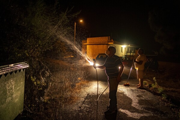 Residents cool their houses with water to prevent it from flames as a wildfire advances through the forest in La Orotava in Tenerife, Canary Islands, Spain on Aug. 19, 2023. (AP Photo/Arturo Rodriguez)