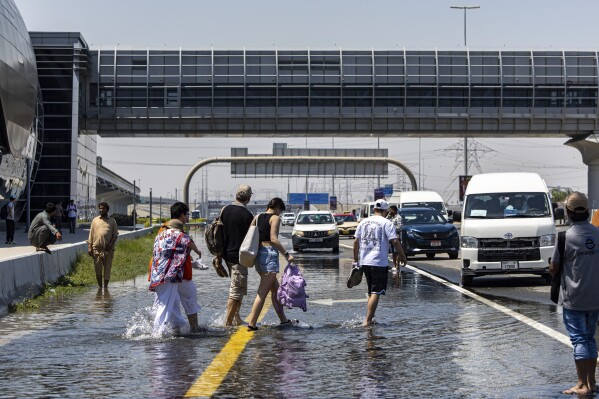 FILE - People walk through floodwater caused by heavy rain while waiting for transportation on Sheikh Zayed Road highway in Dubai, United Arab Emirates, April 18, 2024. A new report says climate change played a role in the floods. (AP Photo/Christopher Pike, File)