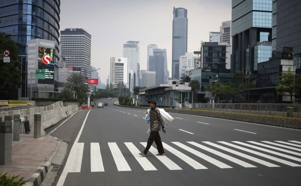 A man crosses a usually traffic-filled Sudirman Street in the main business district in Jakarta, Indonesia, Friday, April 10, 2020. Mosques usually filled for Friday prayers and streets normally clogged with cars and motorcycles were empty as authorities in Indonesia's capital enforced stricter measures to halt the coronavirus' spread after deaths spiked in the past week. (AP Photo/Dita Alangkara)