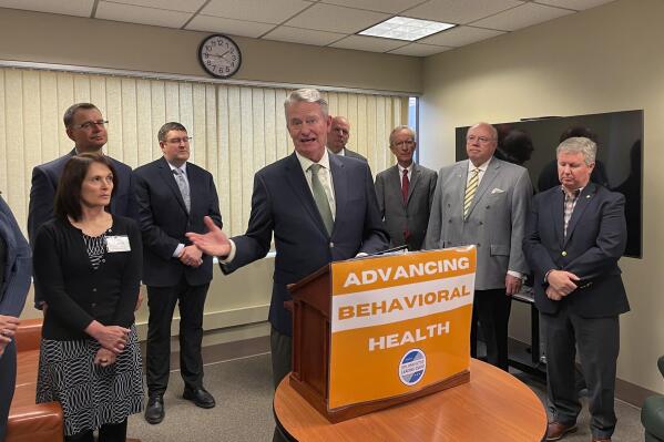 Idaho Gov. Brad Little, at podium, and state officials hold a ceremonial event to mark the passage of some $50 million in investments in behavioral health care by the Legislature that Little signed into law in Boise, Idaho, Tuesday, April 5, 2022. (AP Photo/Keith Ridler)
