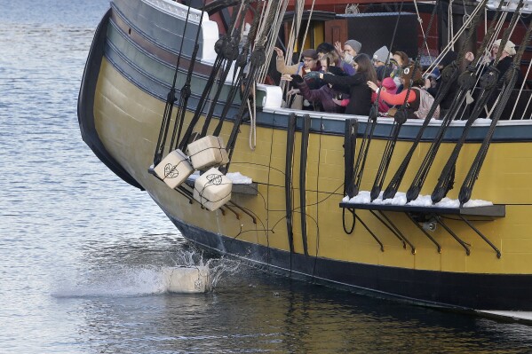 FILE-In this Monday, Dec. 11, 2017 photo, visitors to the Boston Tea Party Museum throw replicas of historic tea containers into Boston Harbor from aboard a replica of the vessel Beaver, in Boston. Patriotic mobs and harbor tea dumping are returning to Boston on Saturday, Dec. 16, 2023, as the city marks the 250th anniversary of the revolutionary protest that preceded America’s independence. (AP Photo/Steven Senne, files)