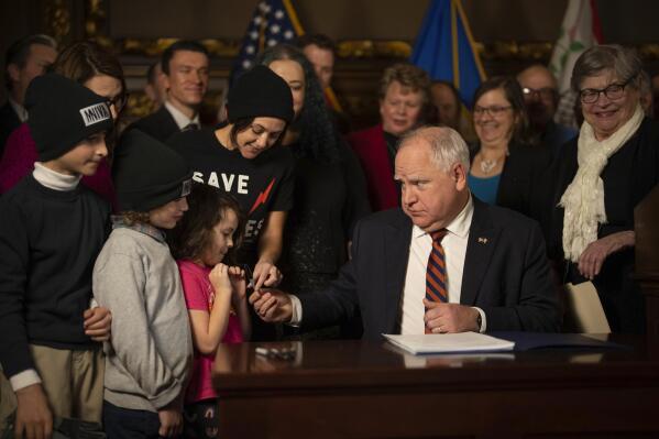 Minnesota Gov. Tim Walz offers the pen he used to sign one of the copies of the federal tax conformity bill to a child in attendance Thursday, Jan. 12, 2023, in the reception room at the state Capitol in St. Paul, Minn. First Avenue President and CEO Dayna Frank accepted it on her behalf. (Jeff Wheeler/Star Tribune via AP)