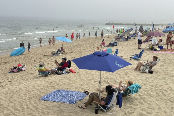 2024年5月26日，周日，新泽西州Ocean Grove海滩上，海滩游客坐在椅子上和雨伞下。阵亡将士纪念日前的一个星期天早上，在一个基督教宗教团体星期天早上关闭海滩的斗争中，几代人第一次来到新泽西州一个海滨社区的沙滩上。（美联社照片/Tasanee Vejpongsa）