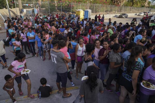 FILE - In this Aug. 30, 2019, file photo, migrants, most of who are asylum seekers that have been sent back to Mexico under the Migrant Protection Protocols, to wait for their asylum cases, stand in line to get a meal in an encampment near the Gateway International Bridge in Matamoros, Mexico. The Supreme Court has ordered the reinstatement of the "Remain in Mexico" policy, saying that the Biden administration likely violated federal law by trying to end the Trump-era program that forces people to wait in Mexico while seeking asylum in the U.S.  (AP Photo/Veronica G. Cardenas, File)