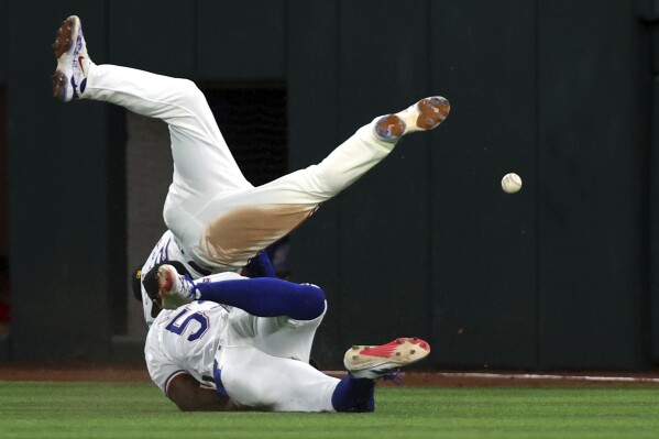 Texas Rangers second baseman Marcus Semien (2) and right fielder Adolis Garcia (53) collide while chasing ball hit by Los Angeles Angels Taylor Ward in the sixth inning of a baseball game Saturday, May 18, 2024, in Arlington, Texas. (AP Photo/Richard W. Rodriguez)