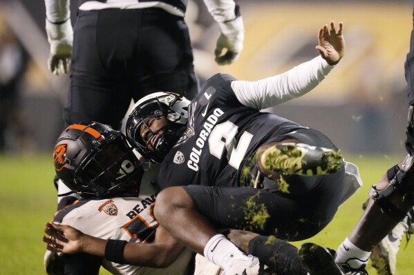 FILE - Oregon State linebacker Andrew Chatfield Jr., left, pulls down Colorado quarterback Shedeur Sanders in the second half of an NCAA college football game in this file photograph taken Saturday, Nov. 4, 2023, in Boulder, Colo. Deion Sanders is accomplishing what he pledged to do by overhauling his offensive line to better protect his often-hit quarterback son. The Colorado coach reached into the transfer portal and brought in linemen from the University of Houston, Connecticut, Indiana and UTEP. (AP Photo/David Zalubowski, File)