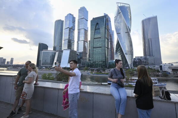 People stroll at embankment of the Moscow River in Moscow, Russia, Tuesday, Aug. 1, 2023, with the 