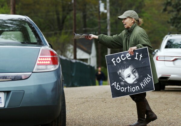 
              Anti-abortion sidewalk counselor Laura Duran, offers reading material to a driver entering the Jackson Women's Health Organization's clinic, the only facility in the state that performs abortions, Tuesday, March 20, 2018, in Jackson, Miss. A federal judge is temporarily blocking a new Mississippi law that bans abortion after 15 weeks, the most restrictive abortion law in the United States. (AP Photo/Rogelio V. Solis)
            